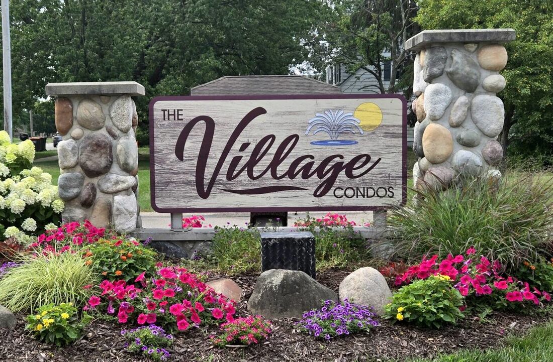 The entrance sign for The Village Condos, set in a bed of hydrangeas and petunias between two fieldstone pillars.